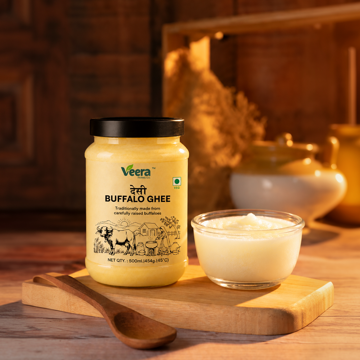 A jar of Veera Buffalo Ghee sits on a wooden board next to a small glass bowl of the ghee and a wooden spoon, set against a warm, rustic background with traditional pottery.